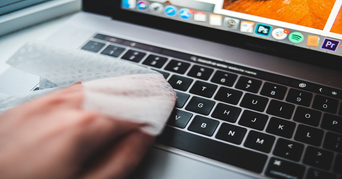 A hand holding a soft cloth preparing to clean a laptop.
